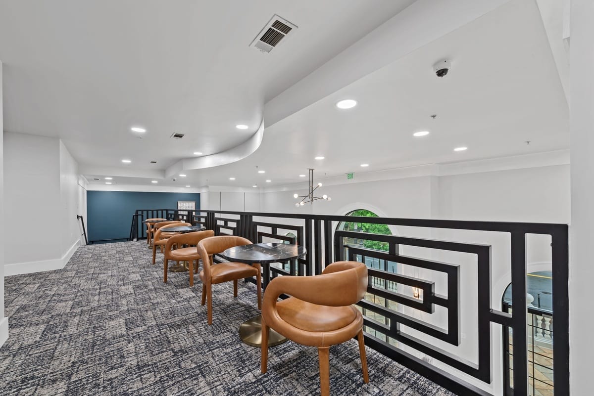 A series of chairs with cafe style tables on the upper level of a room.