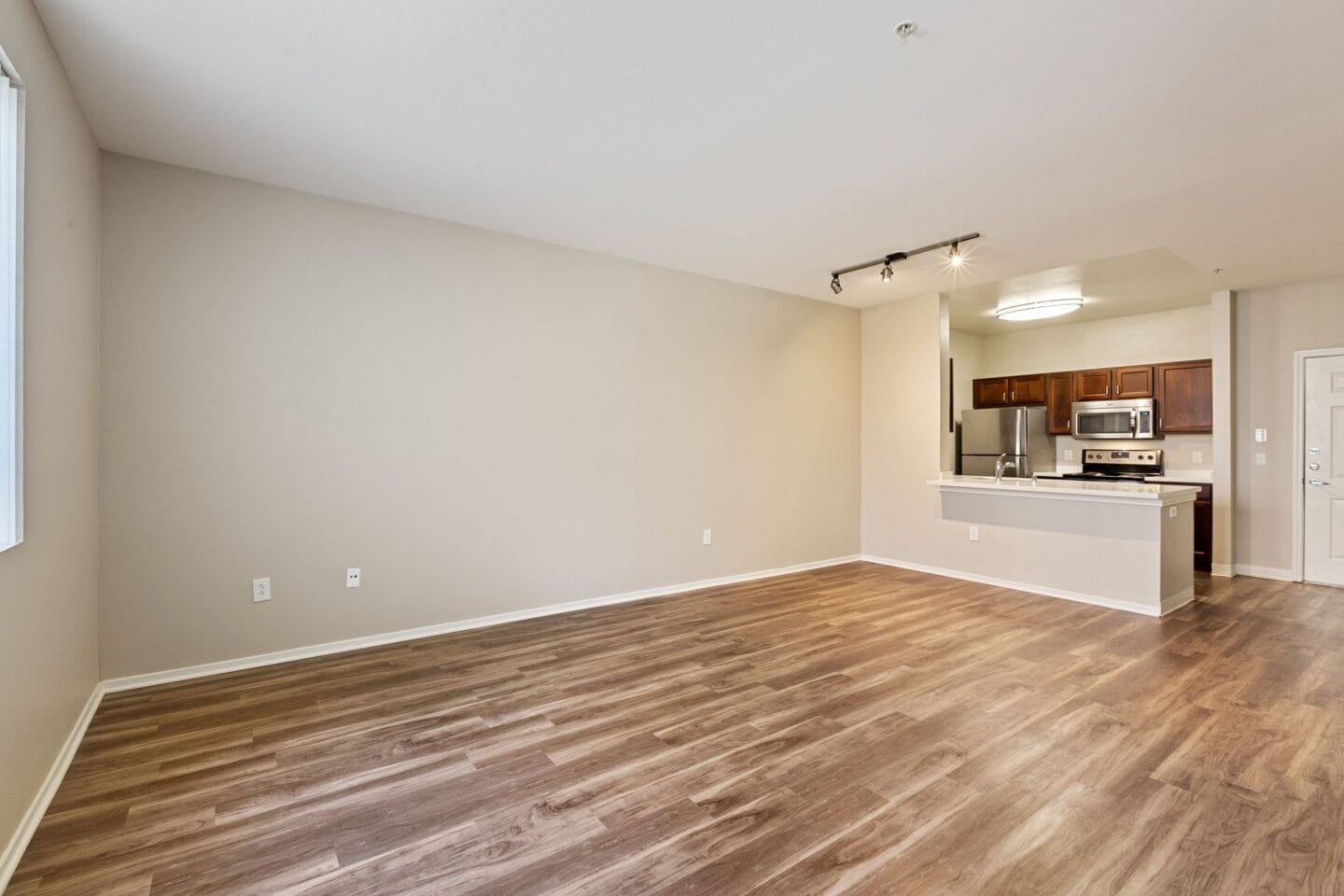 an empty living room with wood flooring and a kitchen