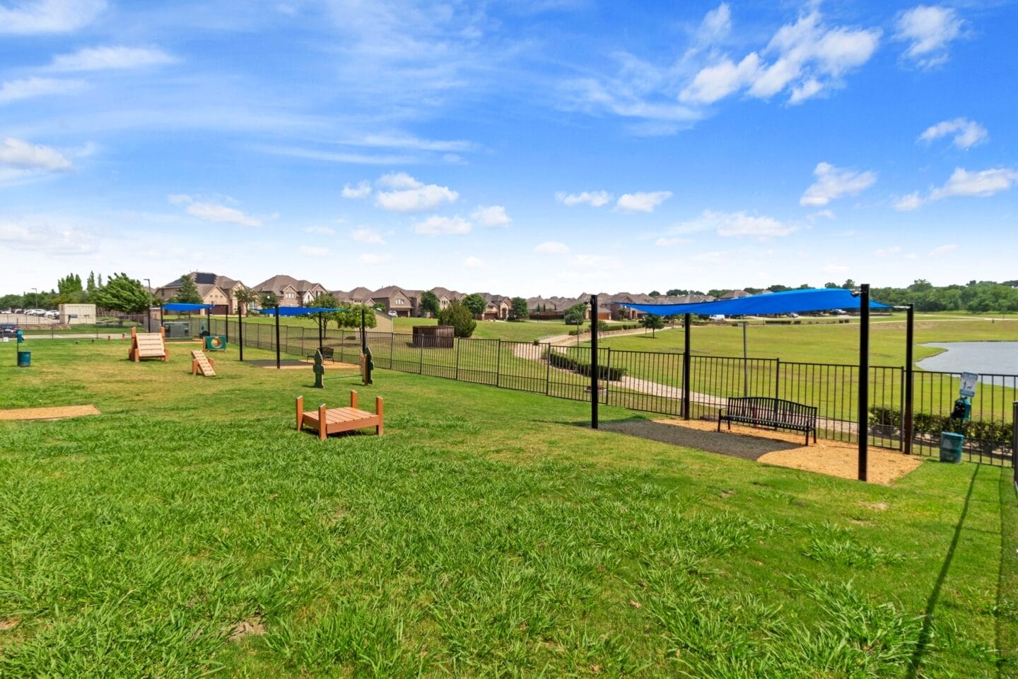 a fenced in dog park with agility courses and a lake