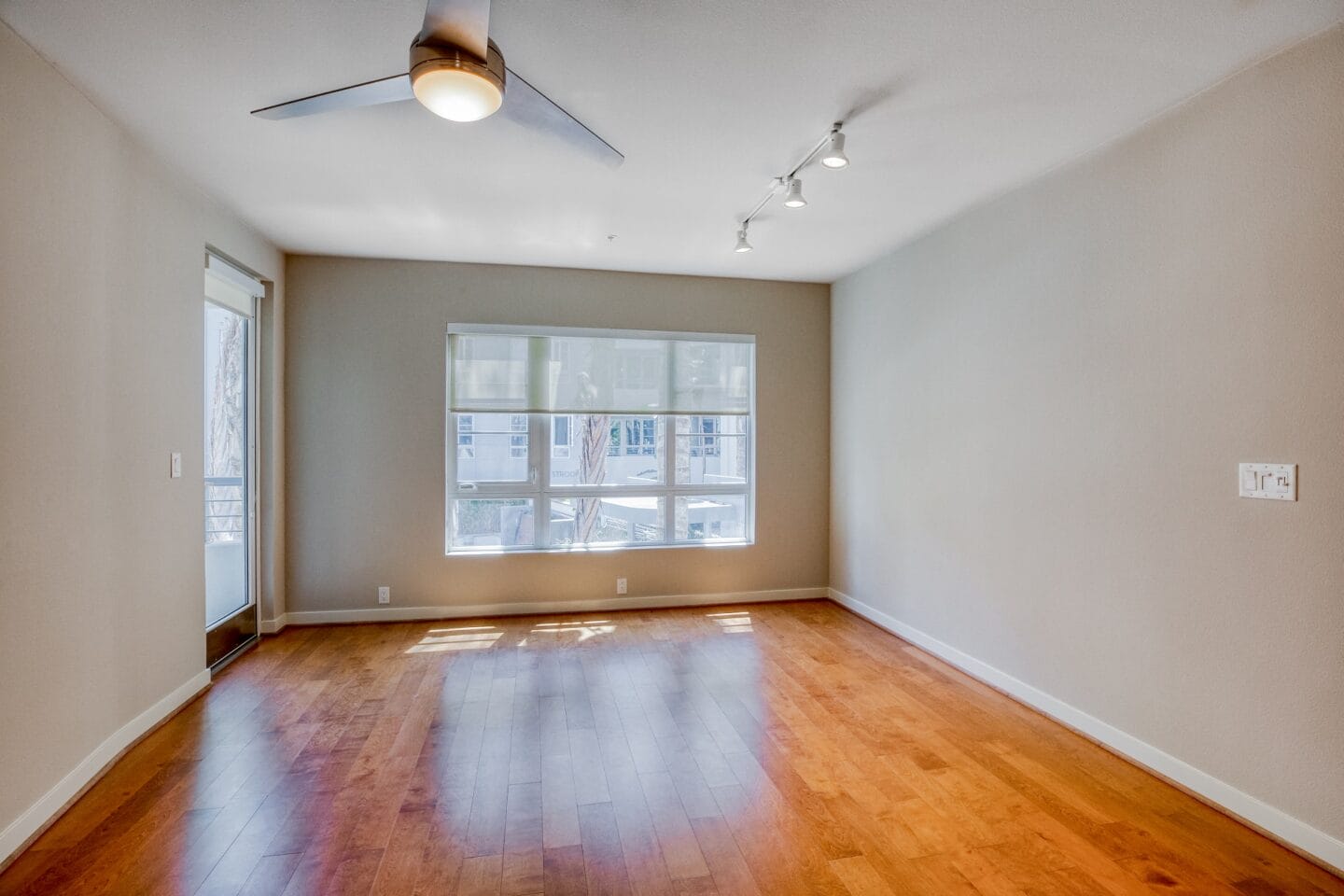 an empty living room with a large window and hardwood floors