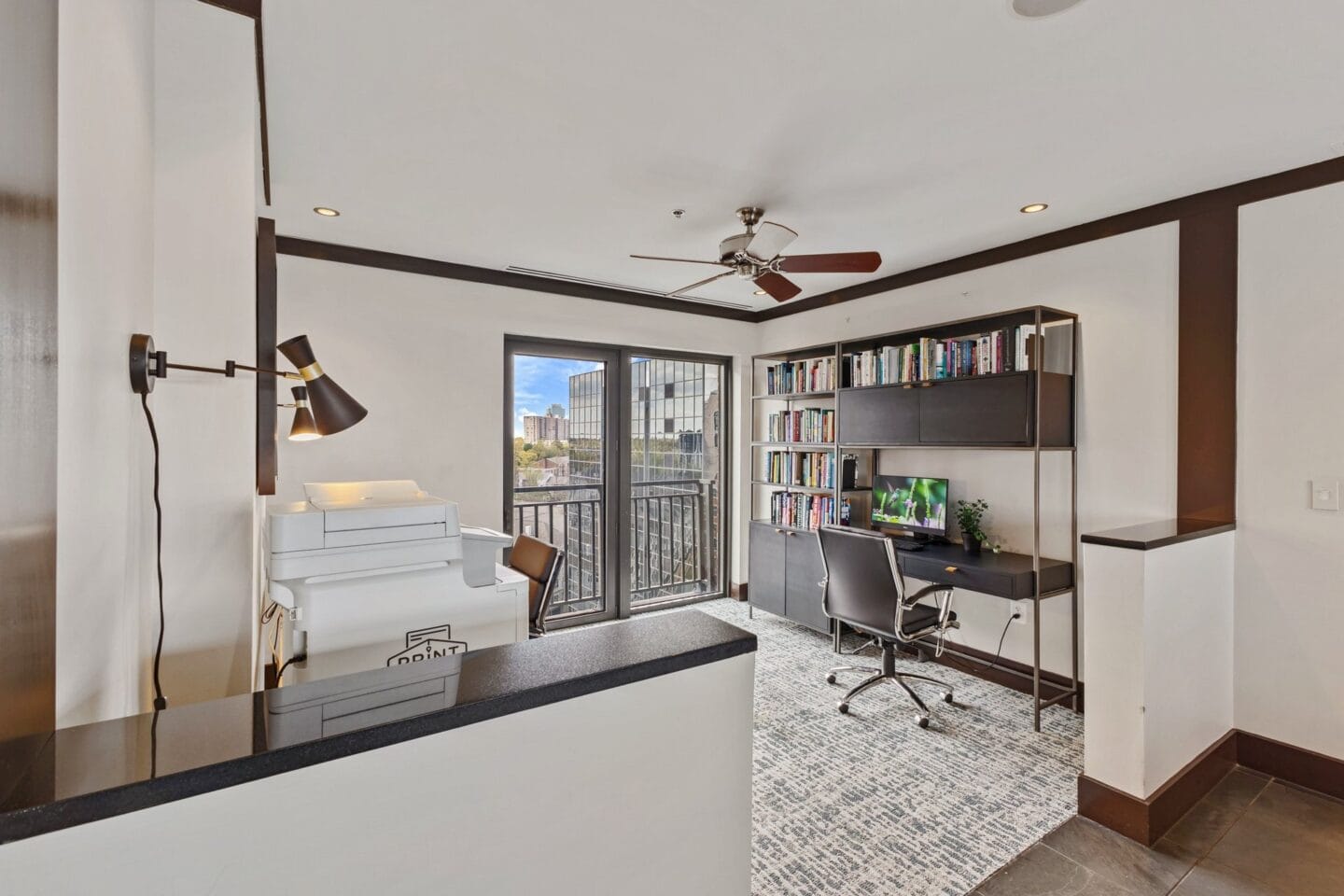 a living room with a desk and a balcony and a ceiling fan