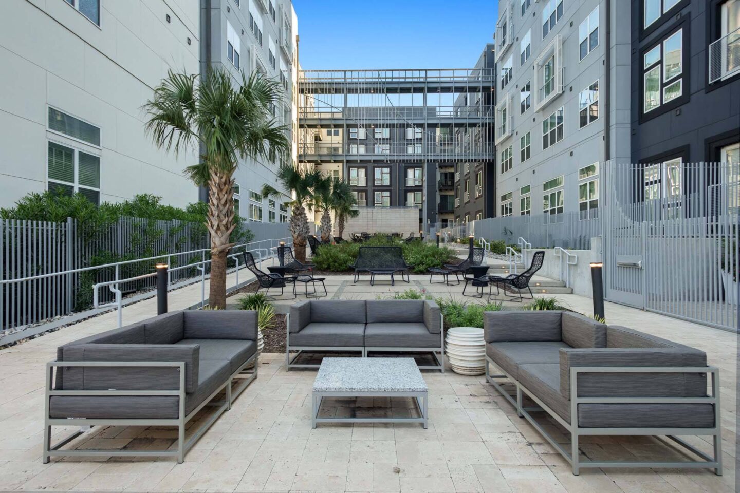 A patio with grey couches and a palm tree at Metro West, Texas, 75024.