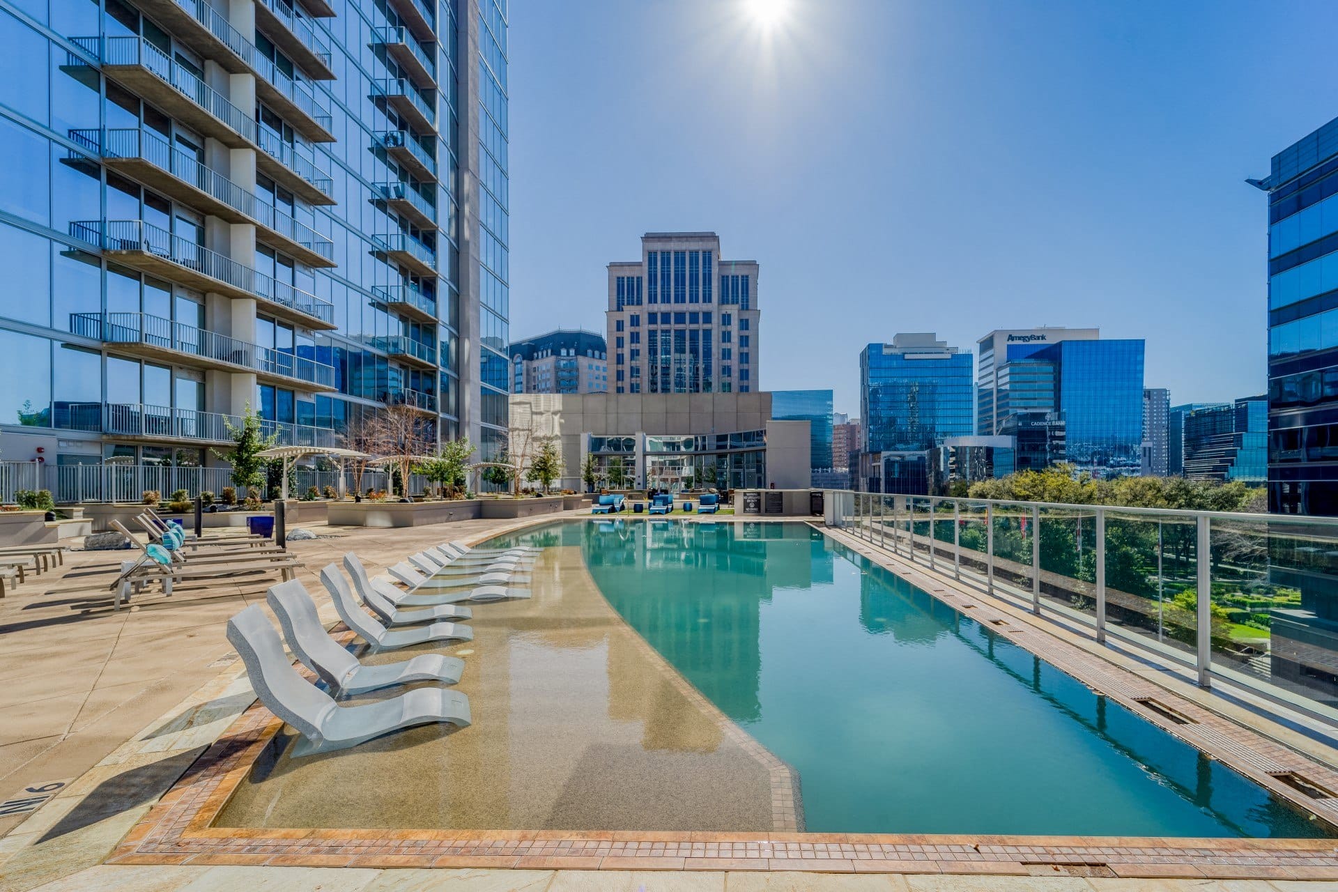 an outdoor pool with chaise lounge chairs and city buildings in the background