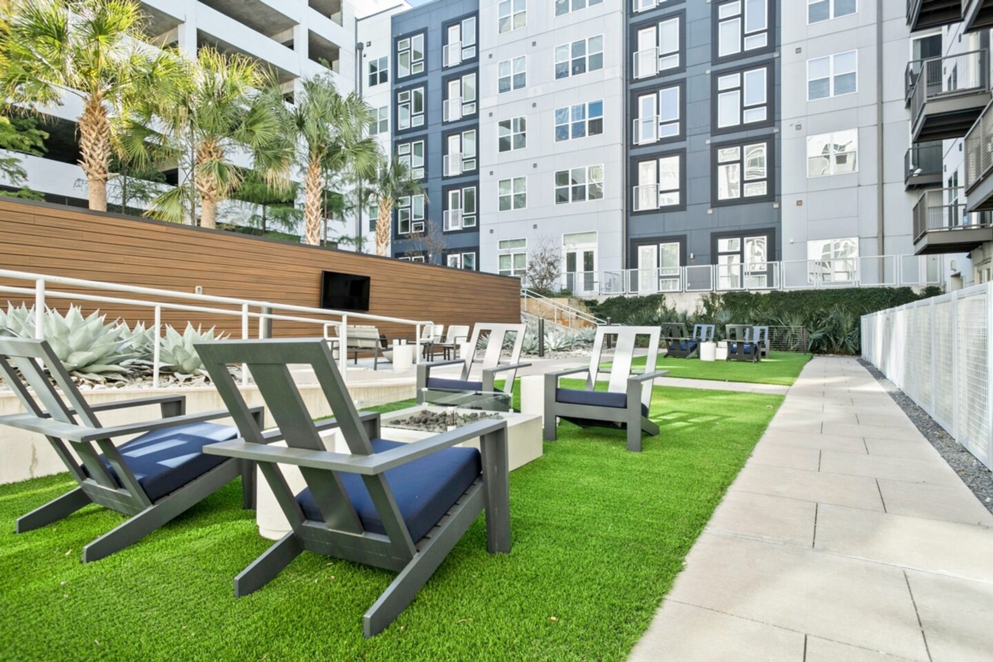 A patio with chairs and a table is surrounded by a grassy area.