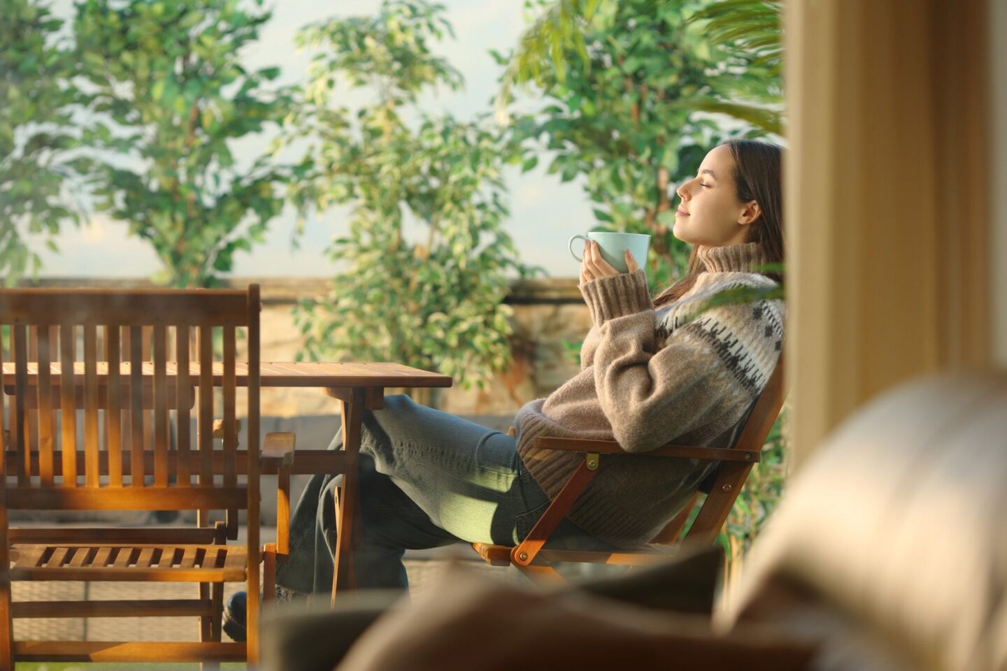 A woman is sitting in a chair on a balcony with a cup in her hand.