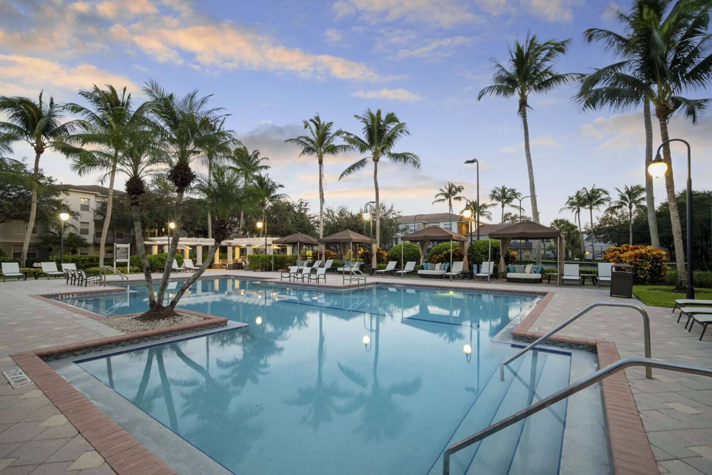 A large swimming pool surrounded by palm trees and lounge chairs at Windsor at Miramar, 3701 SW 160th Ave, Miramar, FL 33027.