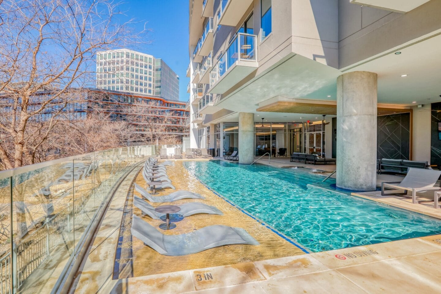 a swimming pool with lounge chairs and a glass walled building in the background