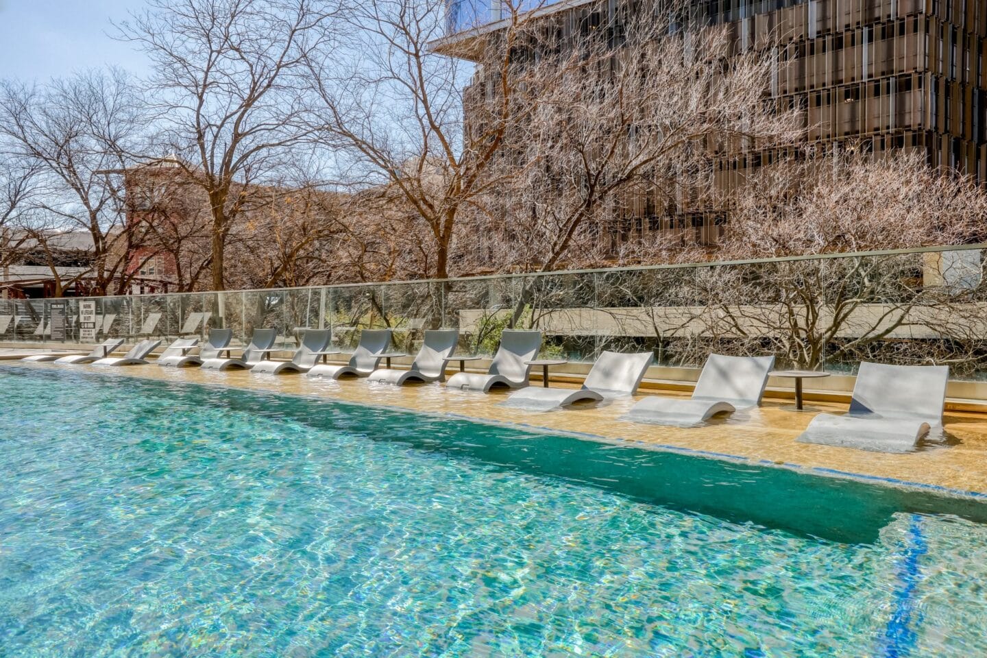 a row of lounge chairs sit at the edge of a pool with a building in the background