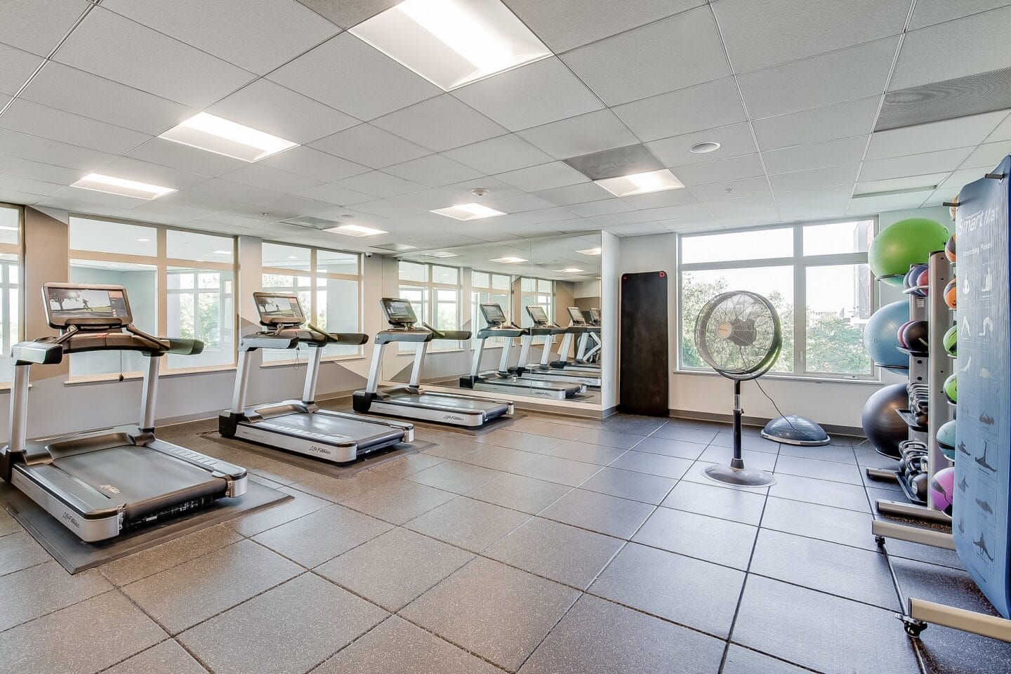 a gym with treadmills and weights in a room with windows