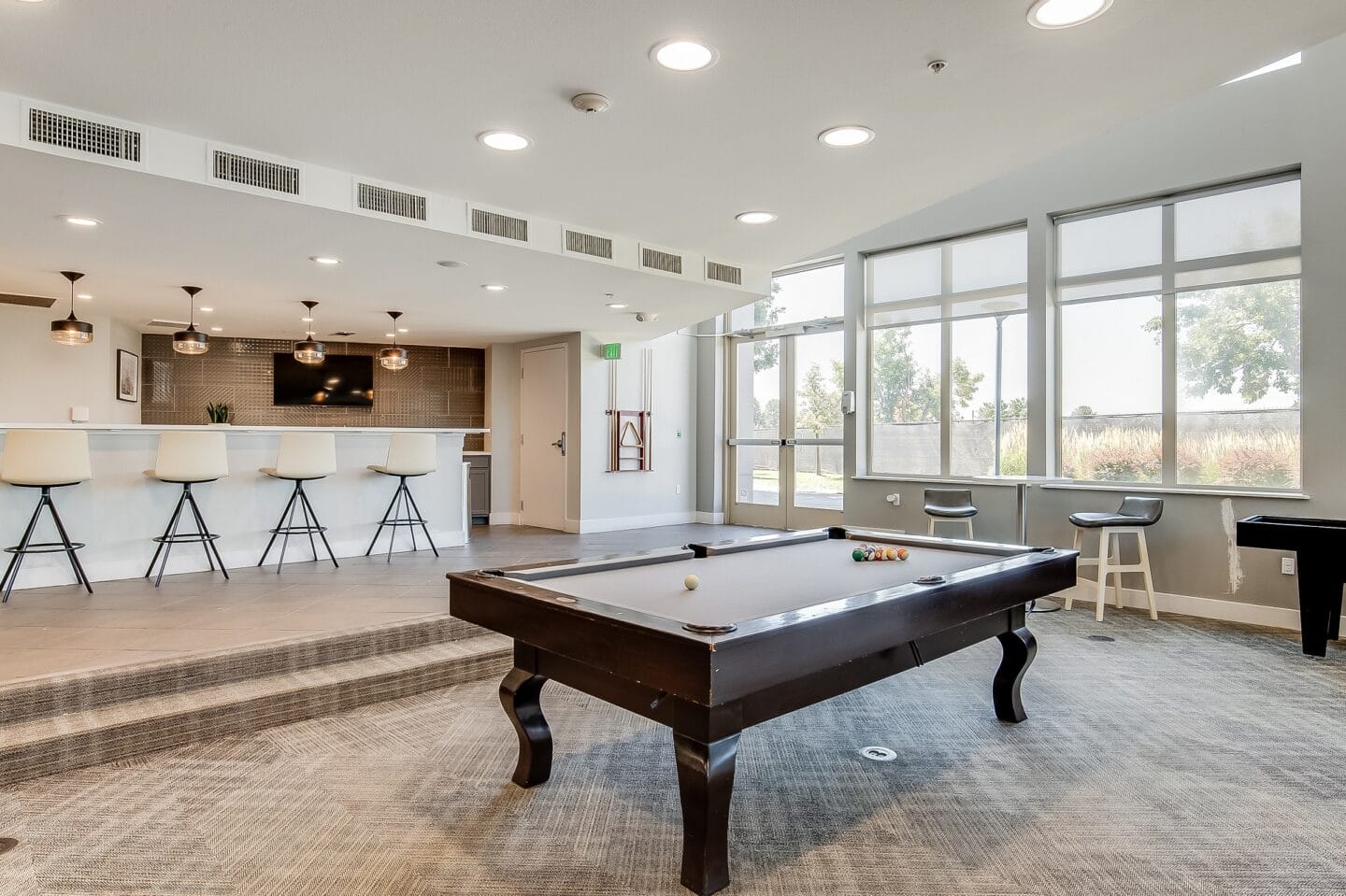 an open living room with a pool table and a bar with bar stools