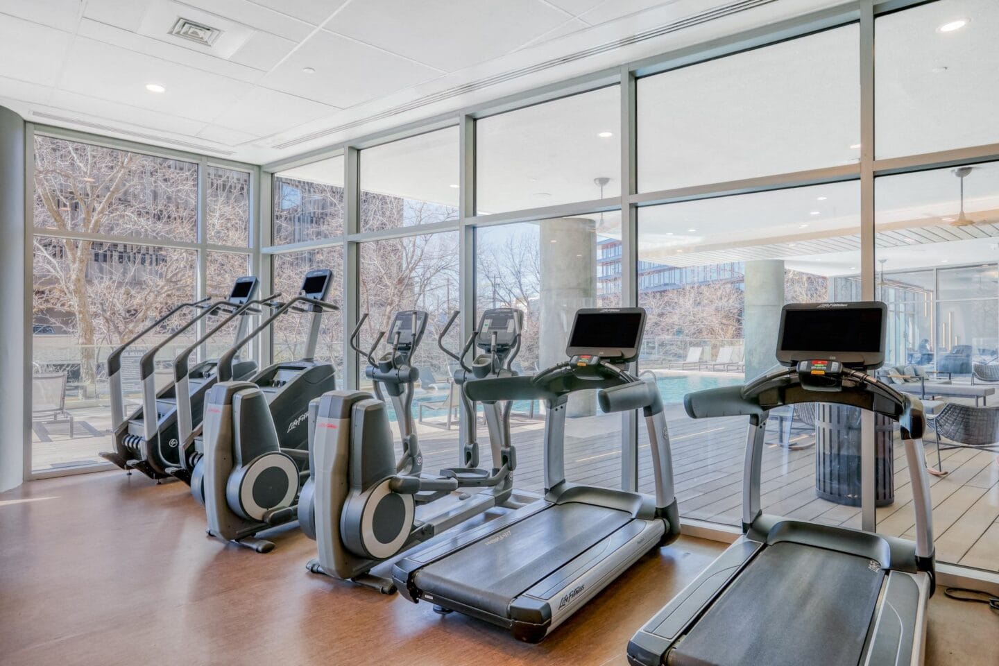 a gym with cardio equipment and large windows