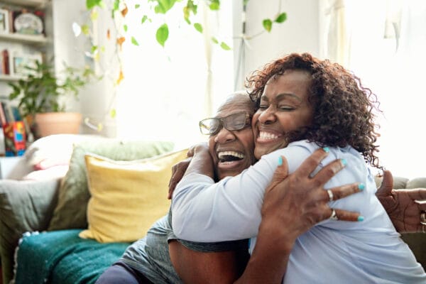 Two women embrace warmly on a couch in a cozy living room, showcasing friendship and comfort in a shared space.