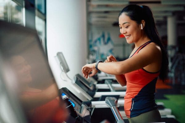 A woman checks her watch while exercising on a treadmill, focused on her workout routine.