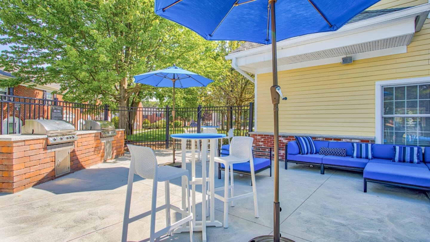 Outdoor patio and grills with blue couches and umbrellas at Windsor Ridge at Westborough, Westborough, MA