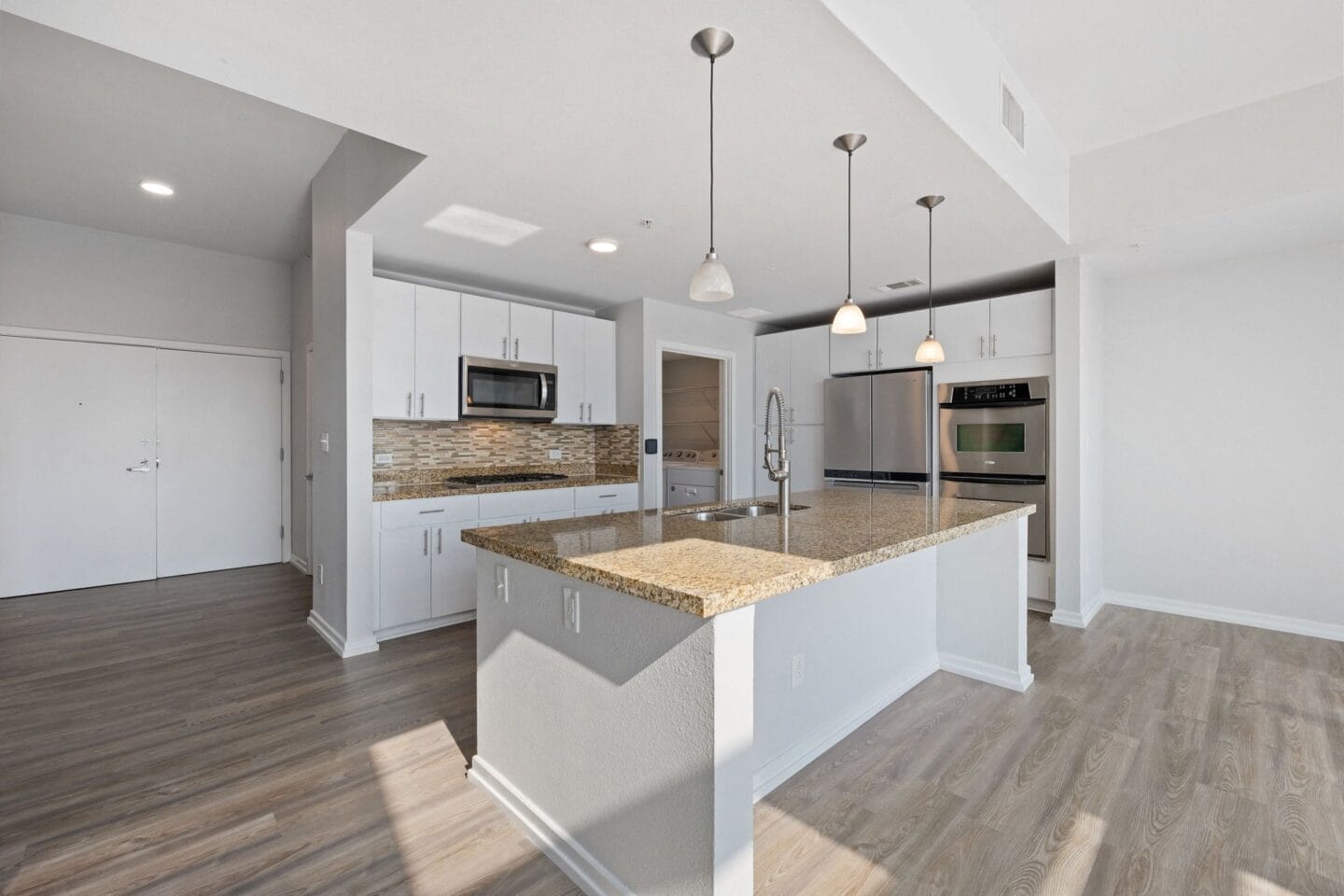 Kitchen with white cabinets and a large island with granite countertops The Monarch by Windsor, Austin, TX