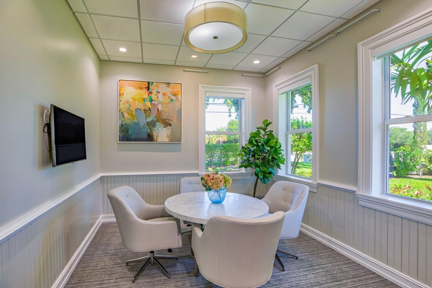 a round table with white chairs and a potted plant in the center of the room