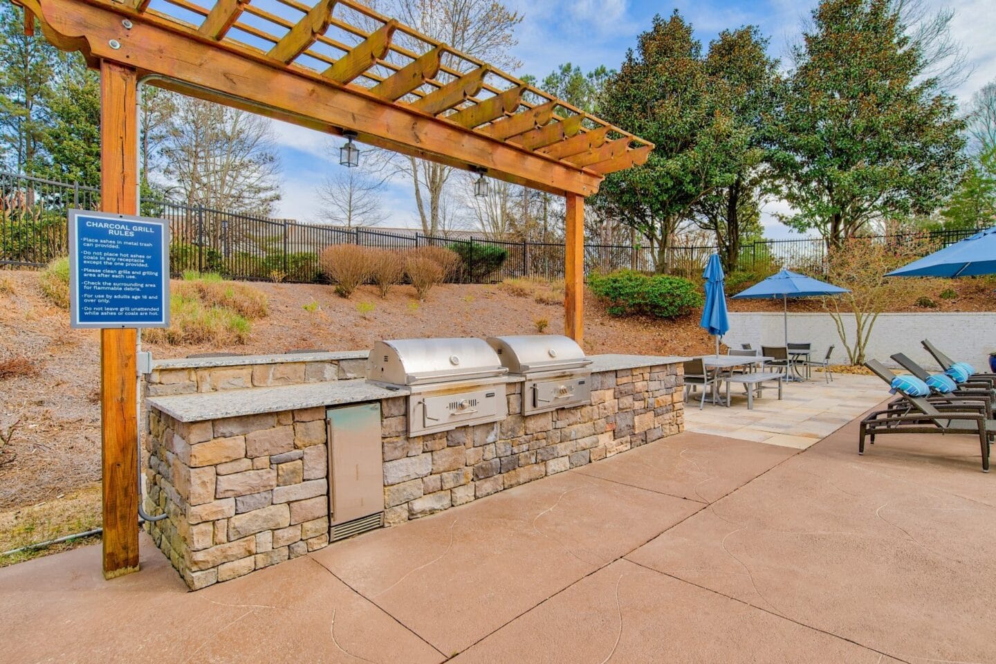 an outdoor barbecue area with a grill and a table with chairs and umbrellas