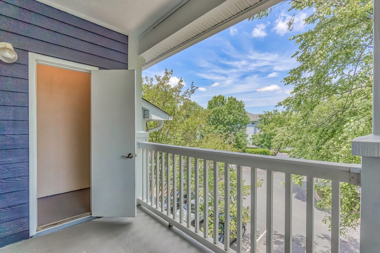 An open door to a balcony with trees and a blue sky in the background