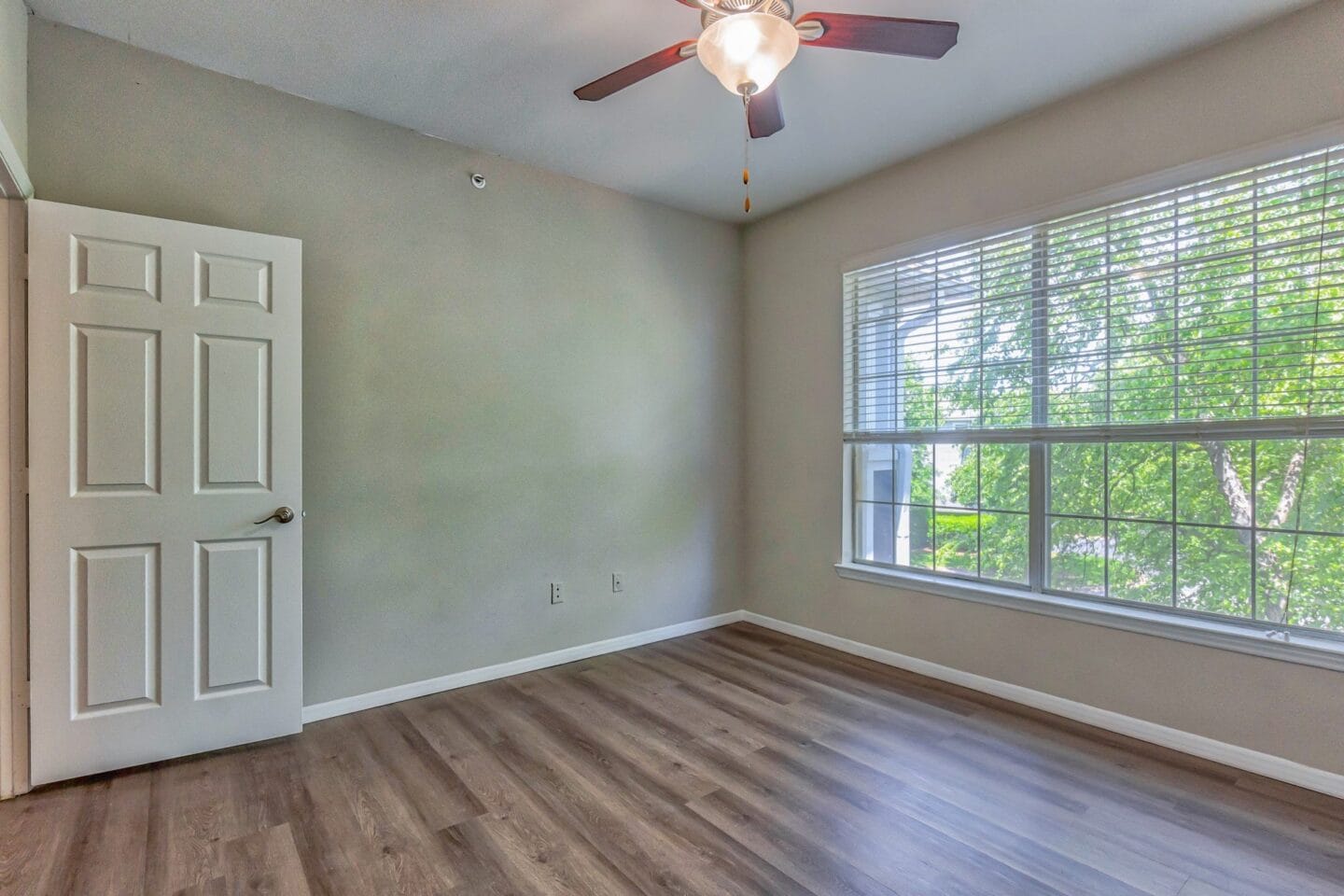 An empty bedroom with a ceiling fan and large windows