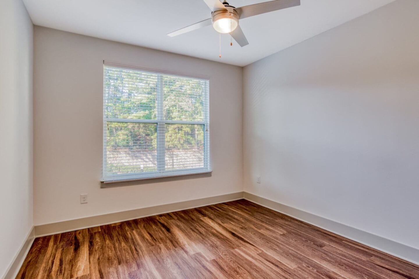 Open vacant room with wood textured flooring and white walls. Big window with blinds