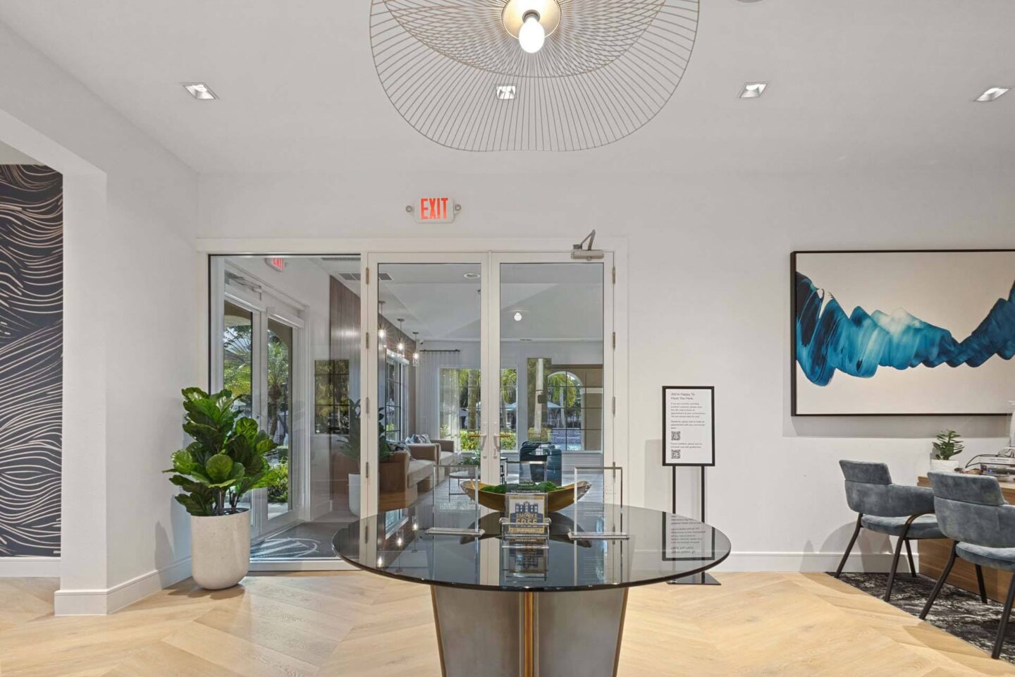 A modern office lobby with a glass table and chairs, a reception desk, and a large abstract painting on the wall.