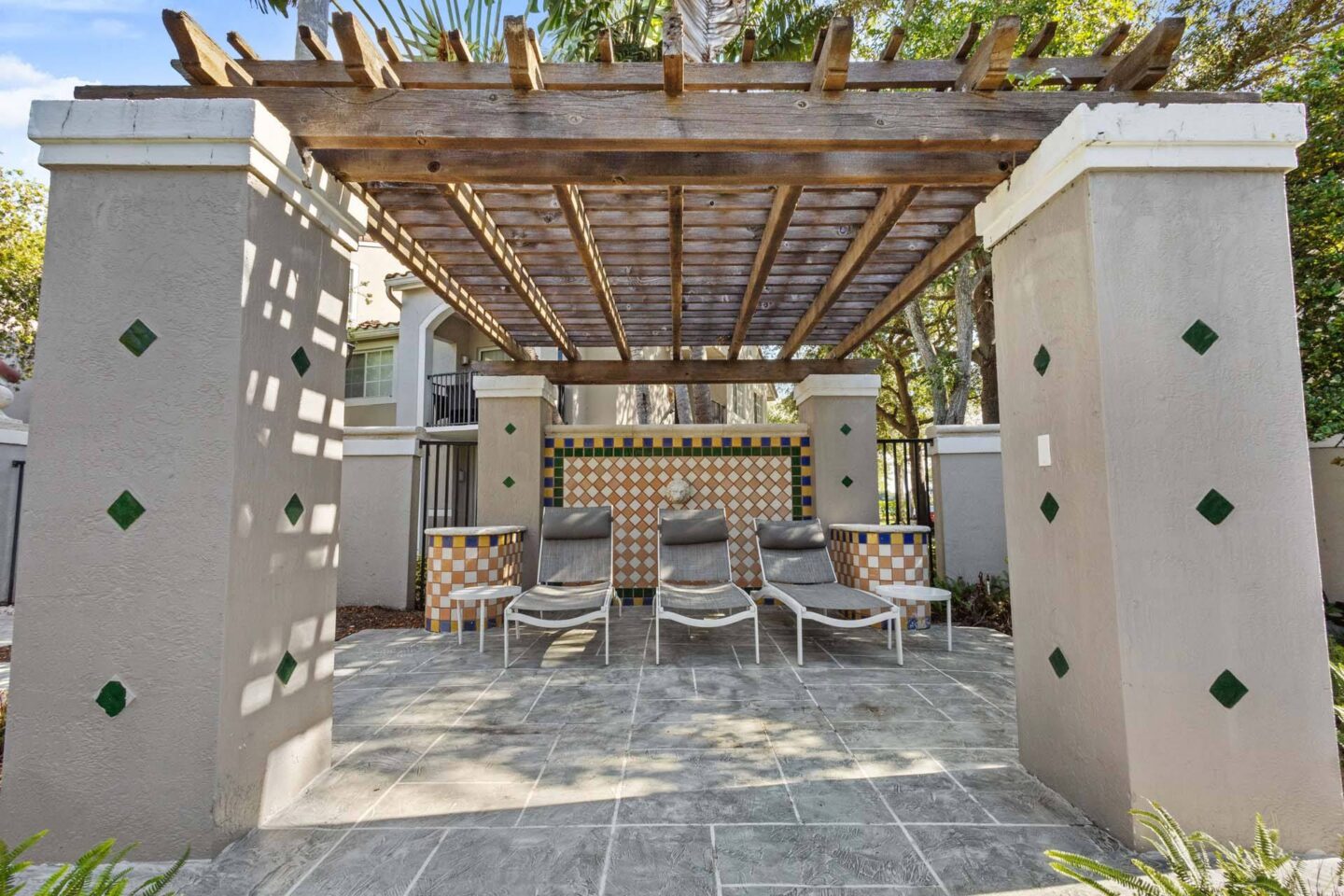 A patio with a wooden pergola and chairs.