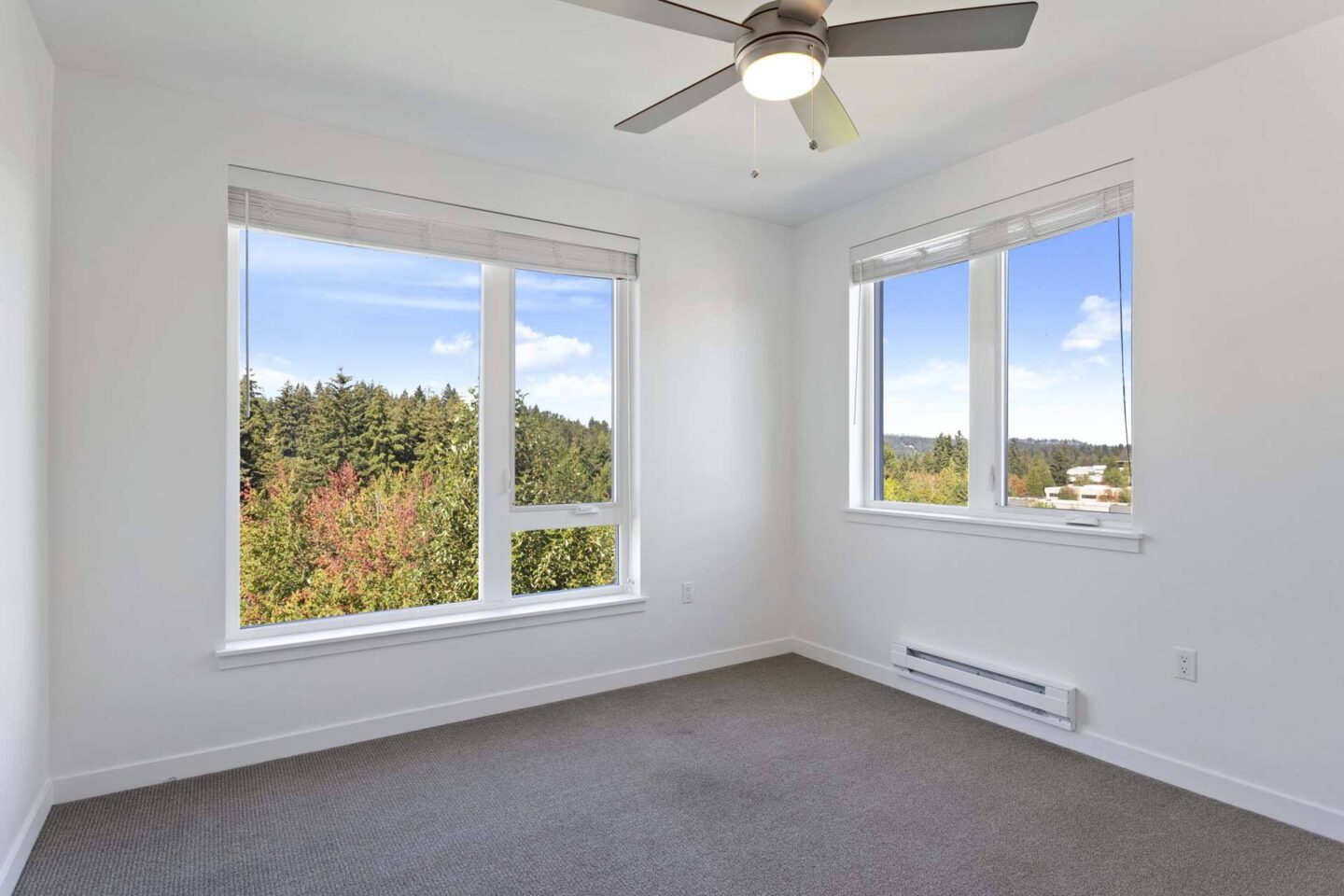 A room with a ceiling fan and two windows overlooking a forest at Windsor Totem Lake, 11723 NE 117th Ct, Kirkland, WA 98034.