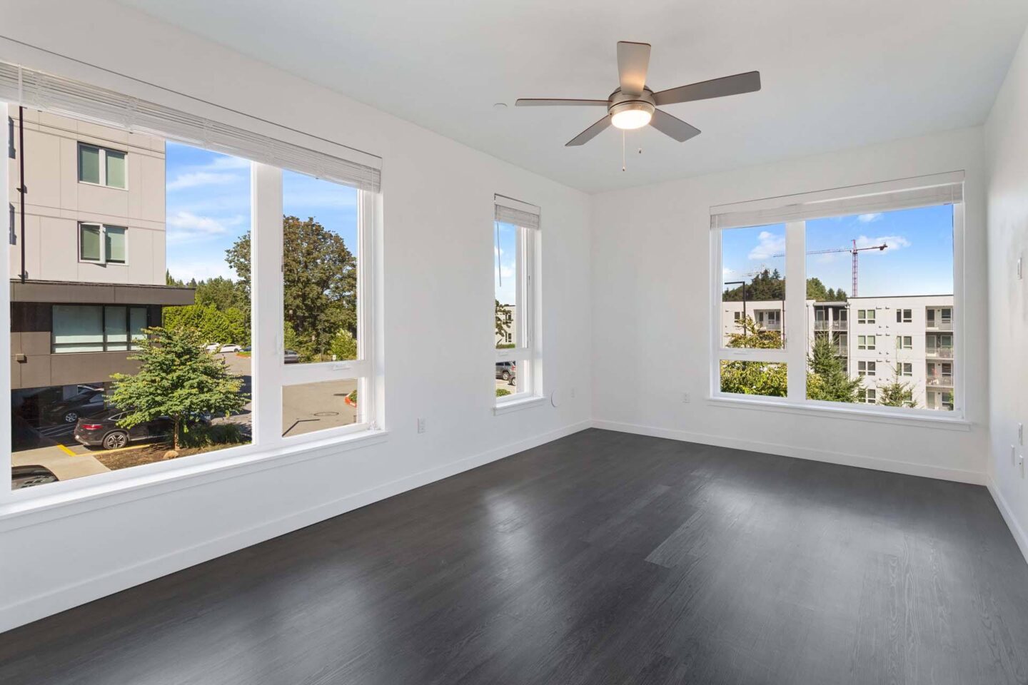 A room with a ceiling fan and large windows overlooking a street at Windsor Totem Lake, 11723 NE 117th Ct, Kirkland, WA 98034.