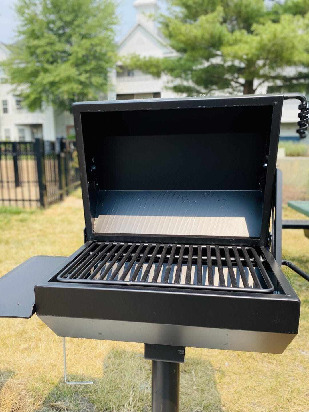 a grill with the lid open on a picnic table in a park