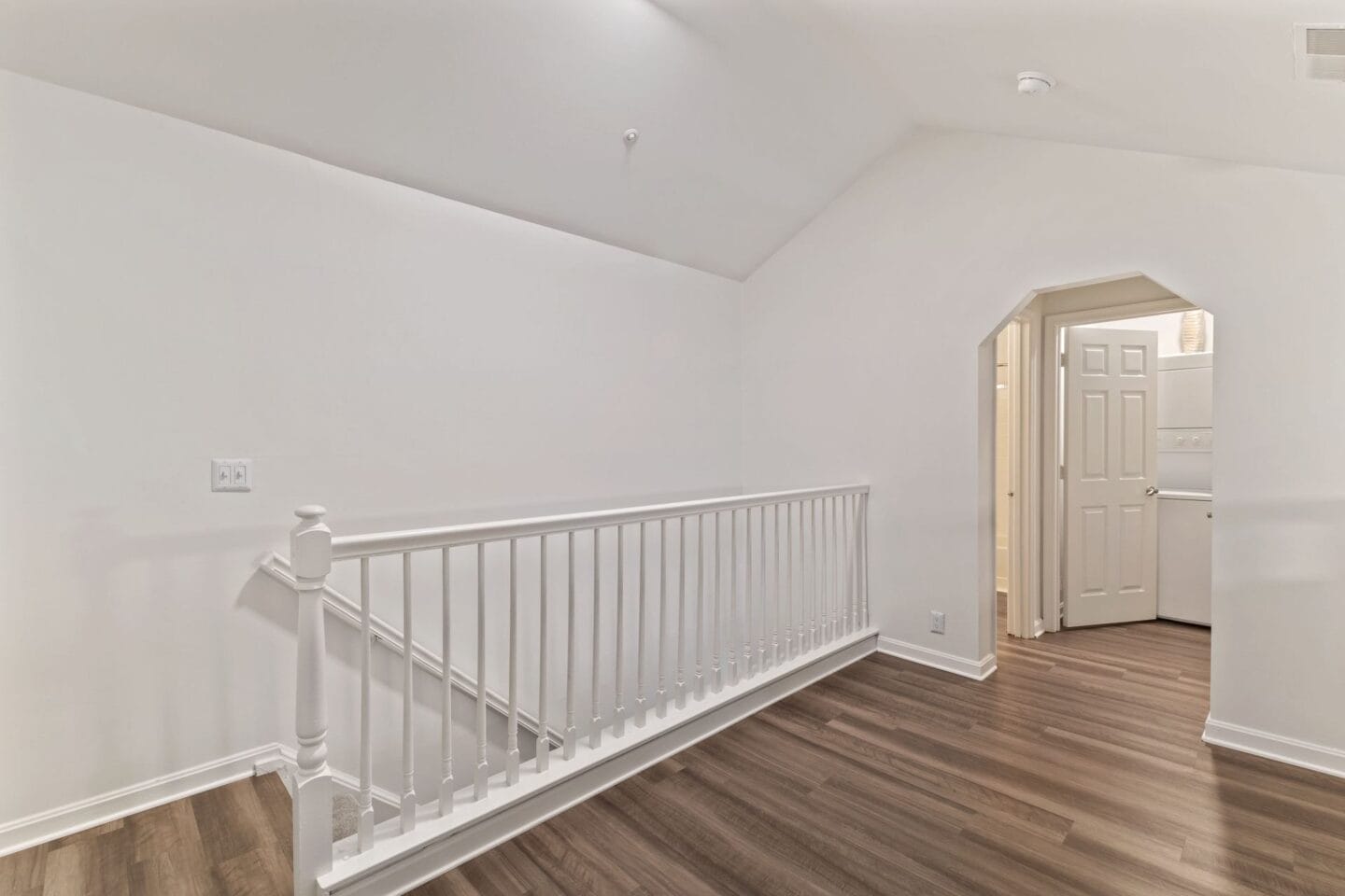 the living room and entryway of a home with white walls and wood floors