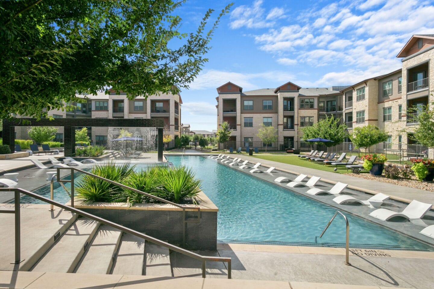 A swimming pool with lounge chairs in front of an apartment building at The Lakeyard District