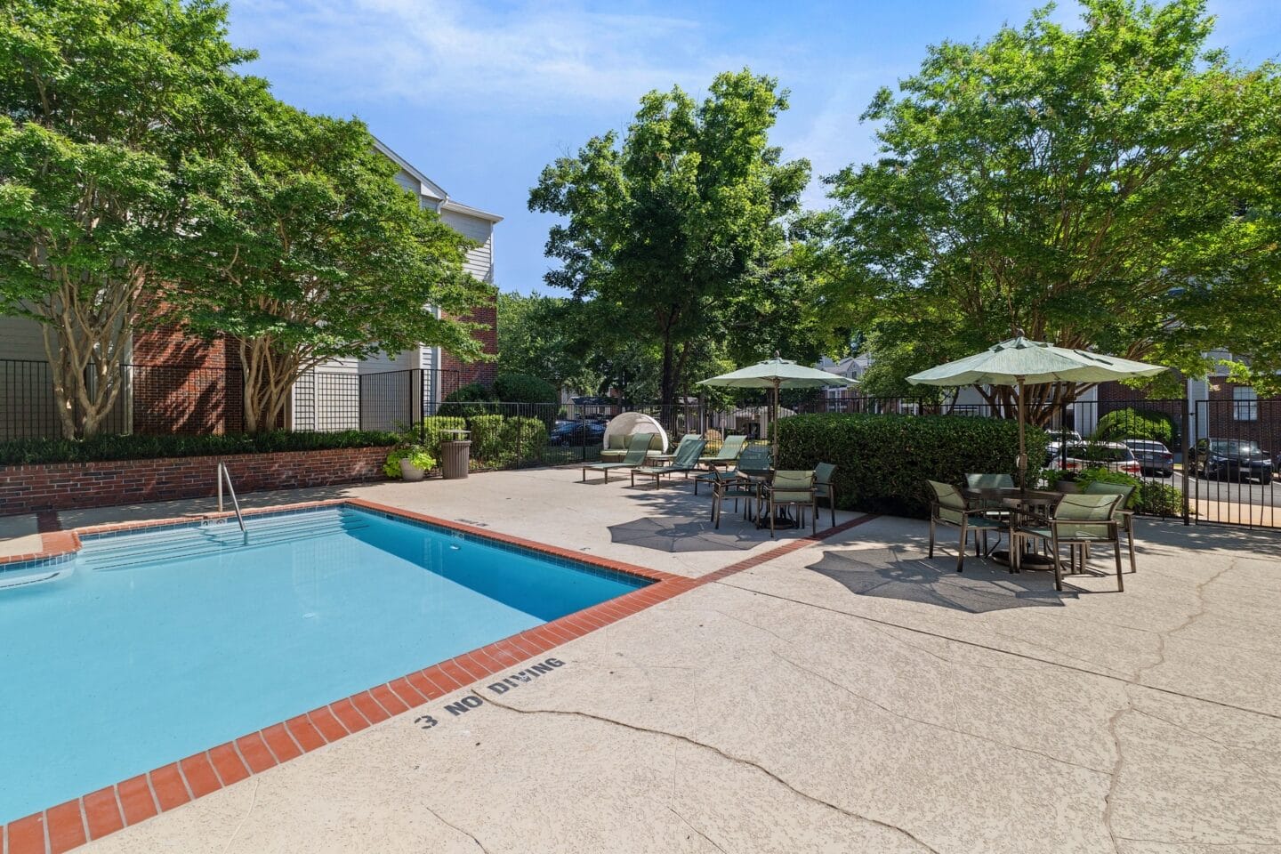 a swimming pool with tables and umbrellas in a courtyard with trees