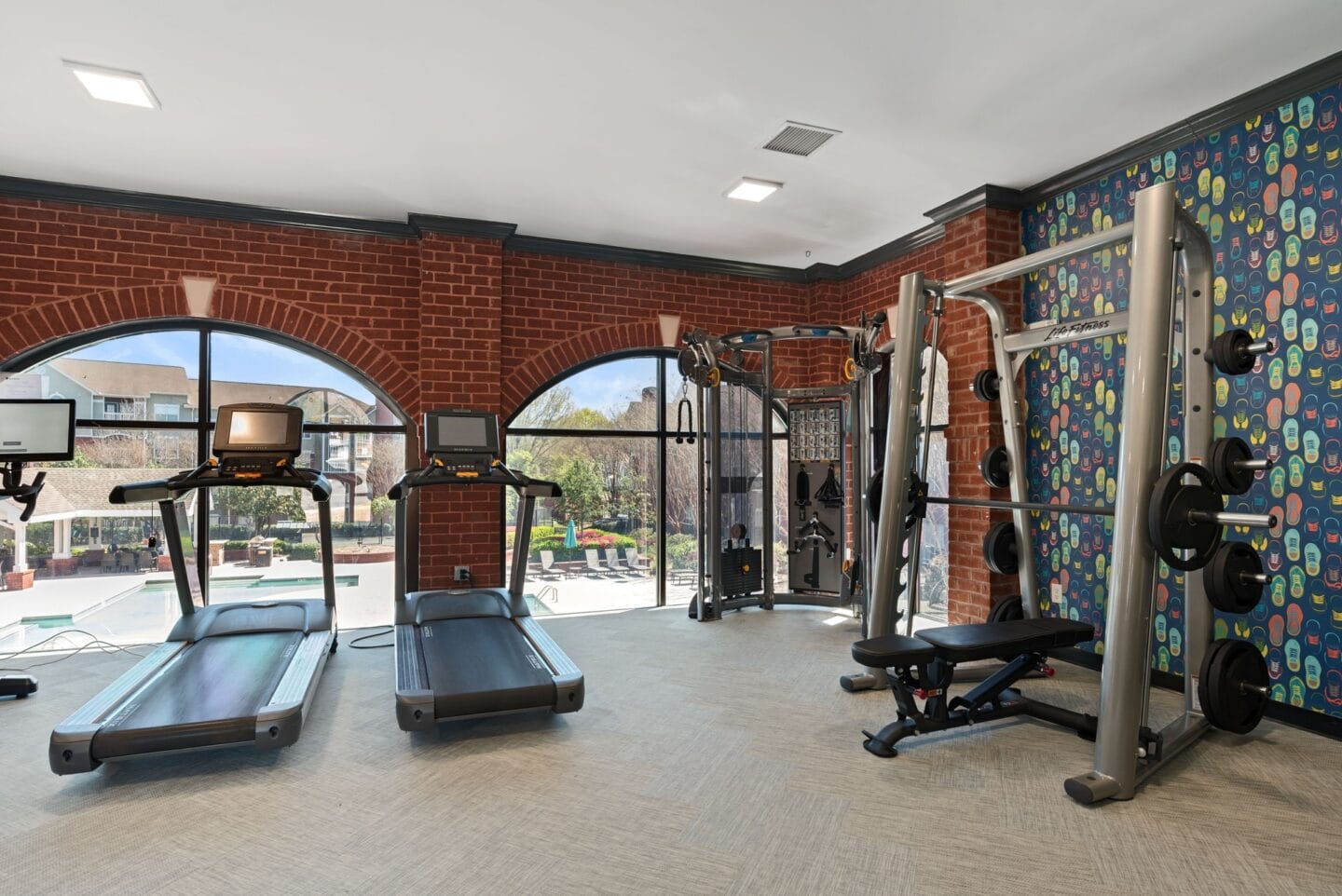 a gym with exercise equipment and windows with a pool in the background