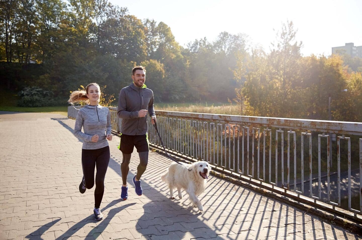 a man and woman running with a dog on a bridge