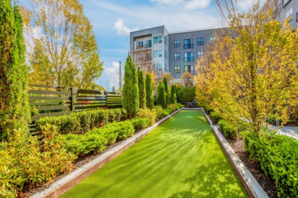 a green lawn with bushes and trees in front of a building