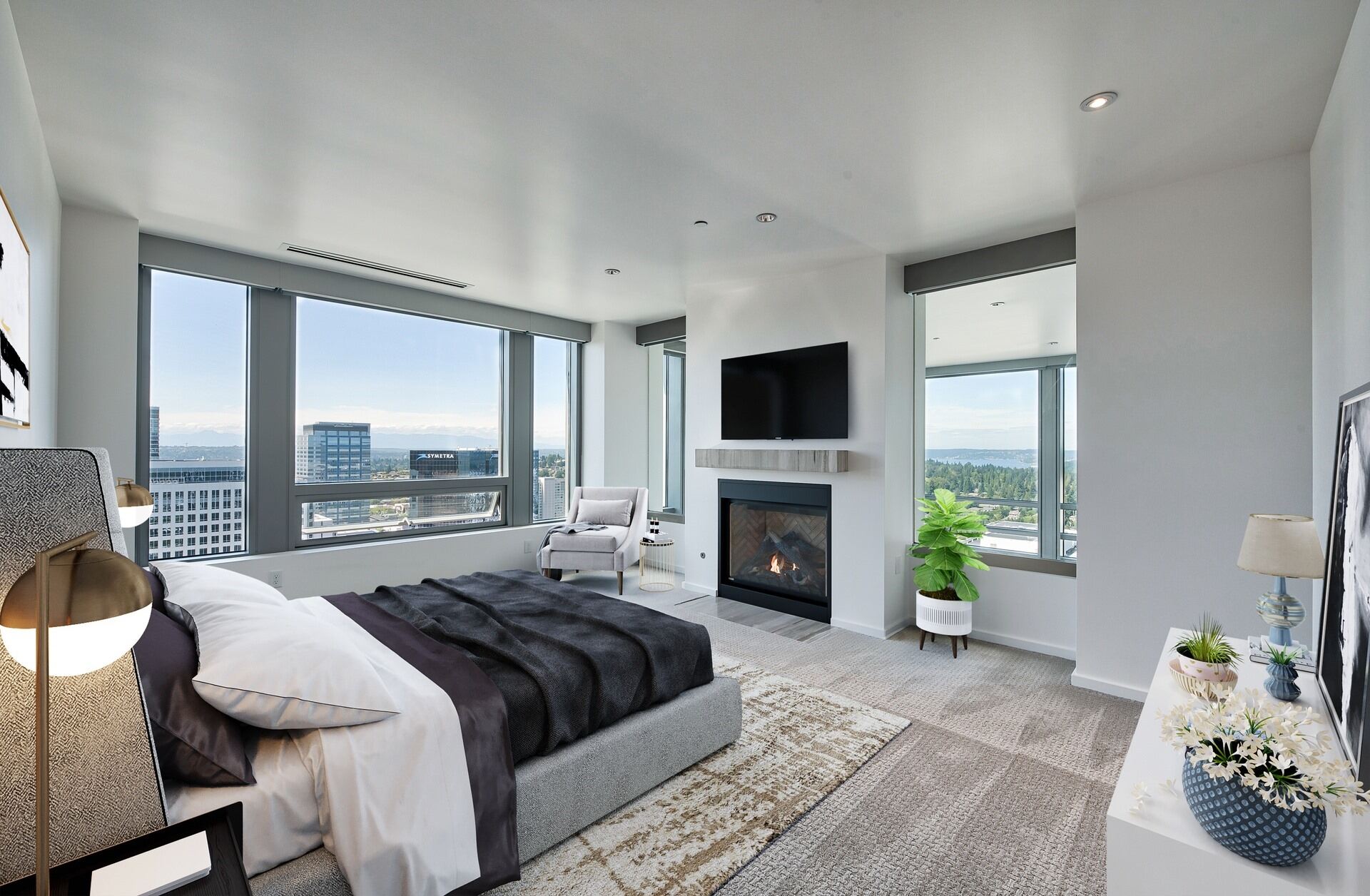 A modern bedroom featuring large windows, a sleek television, and a stylish plant, creating a bright and inviting space