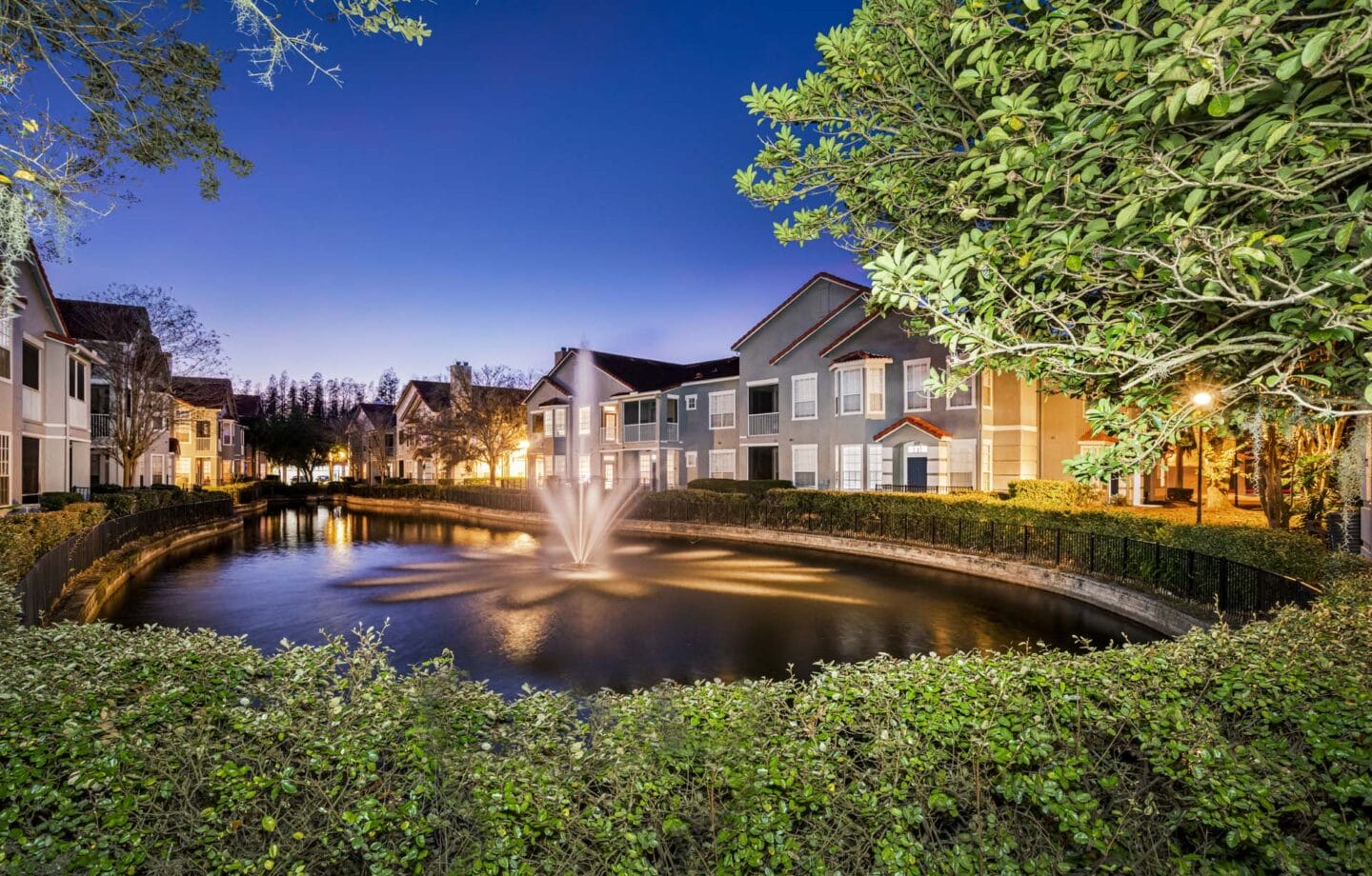 a fountain in a pond surrounded by buildings at night