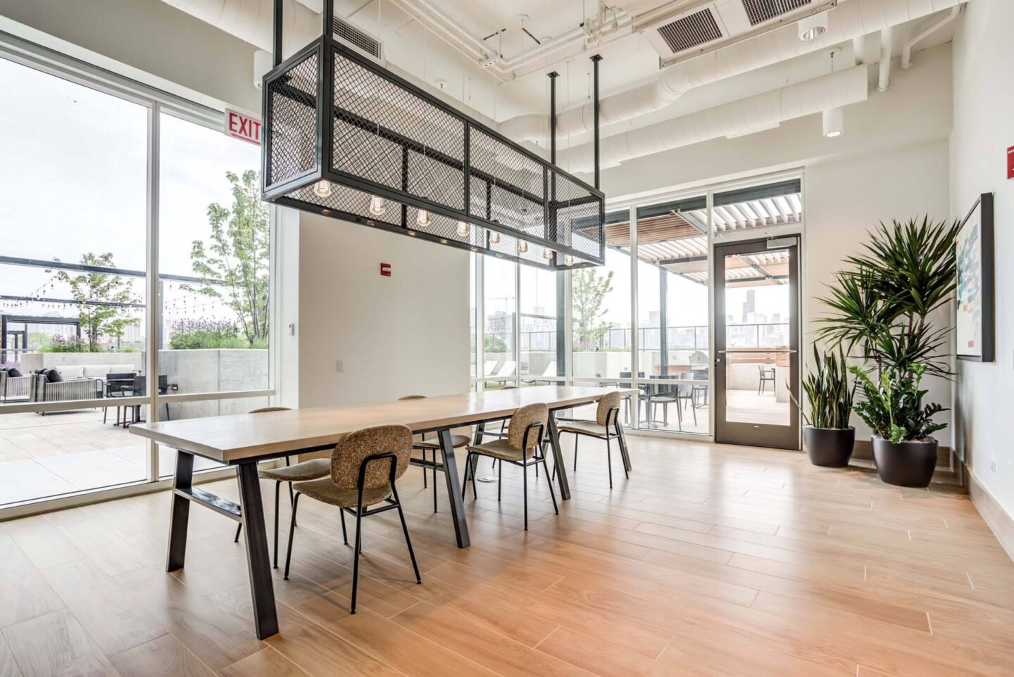 Dining area with a long table and chairs, a hanging light fixture, and a plant on the side at Windsor North + Vine 633 W North Ave, Chicago, IL 60610.