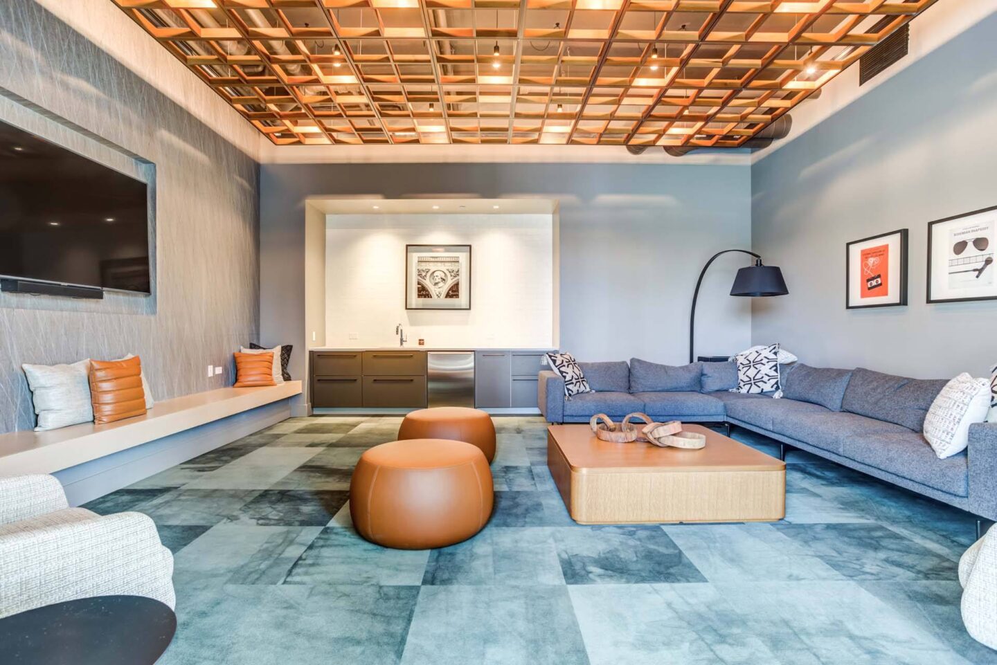 A lounge with a grey couch, a wooden coffee table, and orange poufs at Windsor North + Vine 633 W North Ave, Chicago, IL 60610.