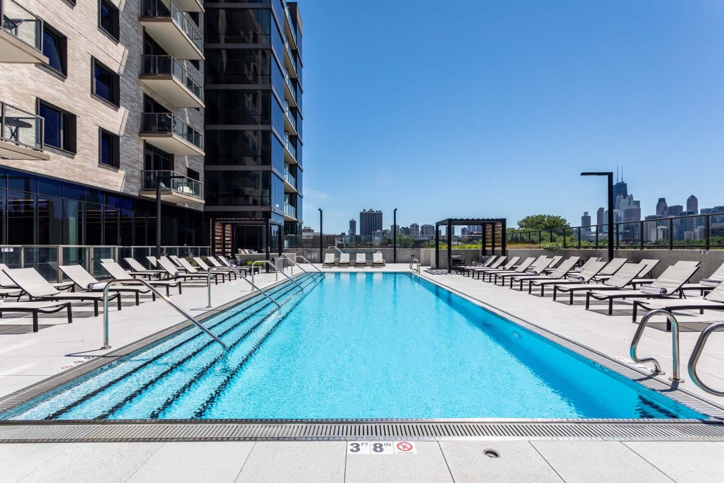 A large blue swimming pool with lounge chairs and a building in the background at Windsor North + Vine 633 W North Ave, Chicago, IL 60610.