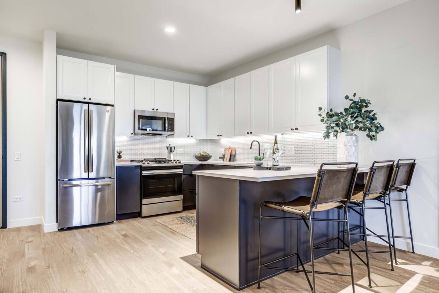 A modern kitchen with a stainless steel refrigerator, microwave, oven, and bar stools.