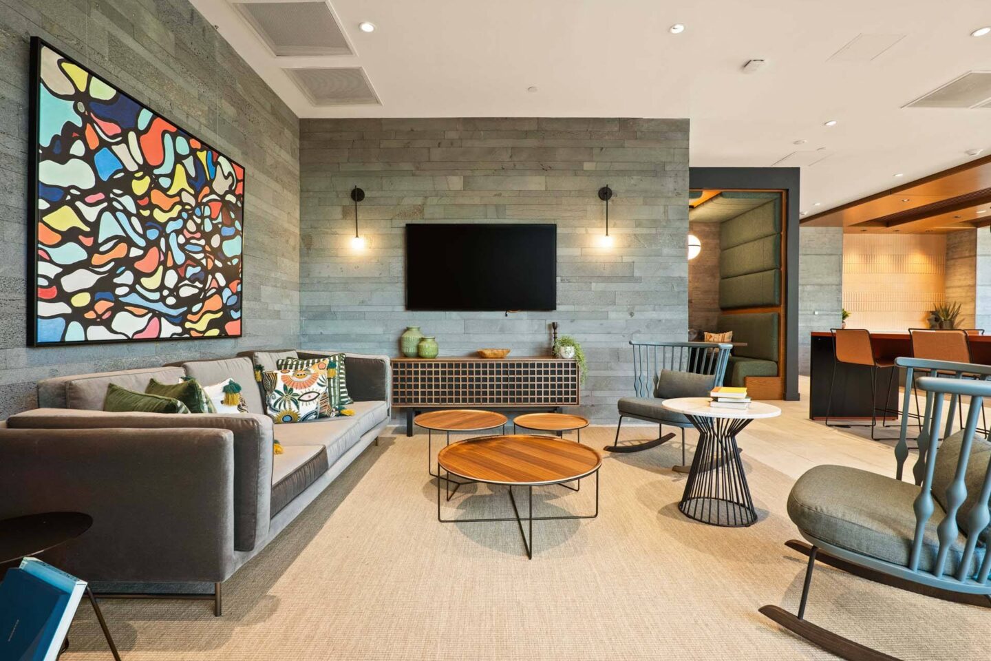 A modern lounge with a grey couch, a wooden coffee table, and a large abstract painting on the wall at Windsor 3000 Huron, 3000. N. Huron Street, Denver, CO 80202.